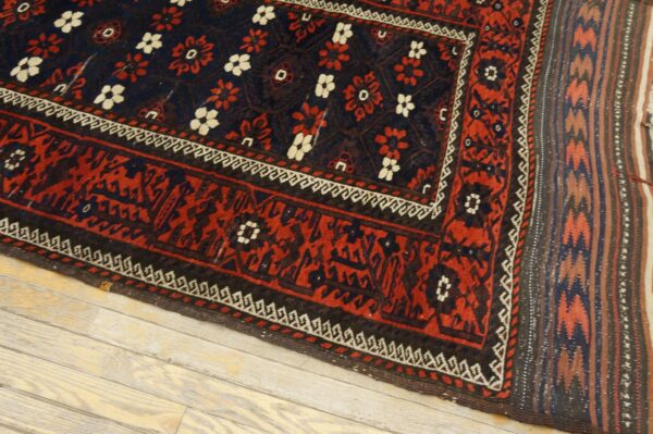 Low-pile rug in navy and red with white flower motifs and complex borders rests on whitewashed wood planks.