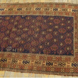 Geometric navy and rust rug with complex tan borders is displayed on light wooden plank flooring.