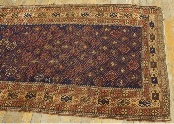 Geometric navy and rust rug with complex tan borders is displayed on light wooden plank flooring.