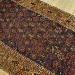 Intricate geometric rug in deep blue, reddish-brown, and gold hues displayed on rustic wooden floorboards.