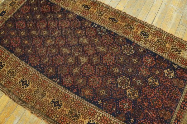 Intricate geometric rug in deep blue, reddish-brown, and gold hues displayed on rustic wooden floorboards.