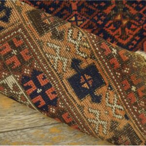 Close-up of a tightly woven, geometric rug in navy, rust, and tan, folded over distressed wood planks.