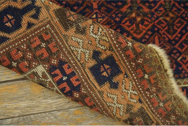 Close-up of a tightly woven, geometric rug in navy, rust, and tan, folded over distressed wood planks.