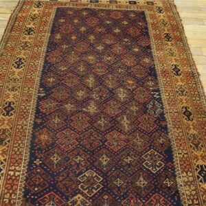 Low-pile navy runner rug with rust and tan geometric patterns displayed on light distressed wooden floors.