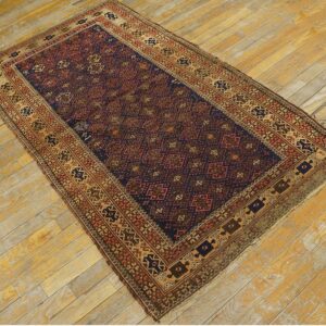 Low-pile rug with navy blue and rust geometric guls and borders on distressed wood floor.