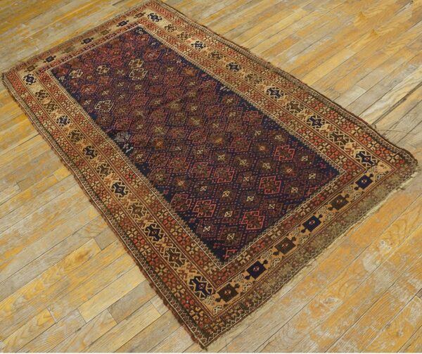 Low-pile rug with navy blue and rust geometric guls and borders on distressed wood floor.