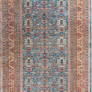 A rectangular runner rug features a teal blue central field with geometric rust and cream motifs, surrounded by a wide peach border.