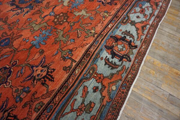 Orange and blue patterned rug with low pile lying on distressed gray wood flooring.