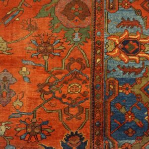 Intricate red and blue patterned rug featuring animals and vines lies close-up on light wooden flooring.