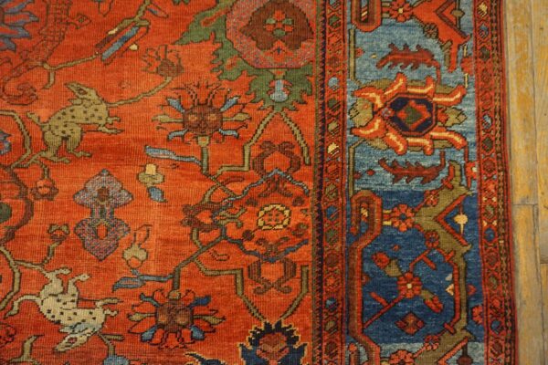 Intricate red and blue patterned rug featuring animals and vines lies close-up on light wooden flooring.