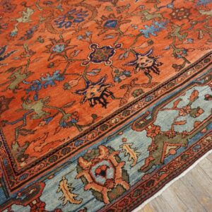 Traditional orange rug featuring an intricate blue and rust border on weathered wood flooring.