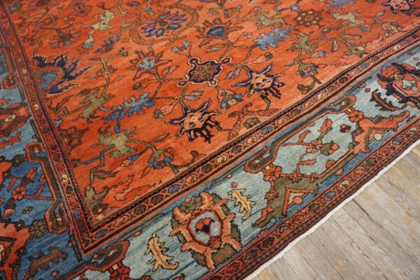 Traditional orange rug featuring an intricate blue and rust border on weathered wood flooring.