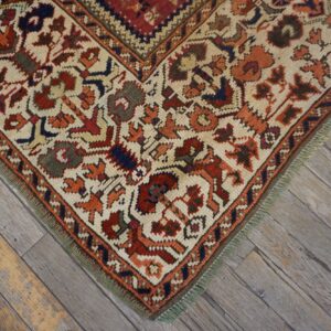 Low-pile rug corner with cream and rust traditional patterns rests on diagonal, worn gray wood planks.