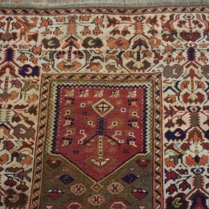 Low-pile rug with geometric patterns in red, cream, olive, and rust sits on distressed wood planks.