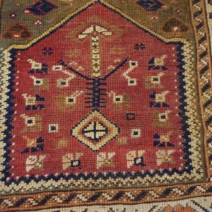A closely cropped, low-pile rug with a red niche motif and geometric patterns in blue, cream, and olive.