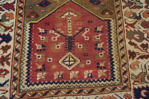 A closely cropped, low-pile rug with a red niche motif and geometric patterns in blue, cream, and olive.