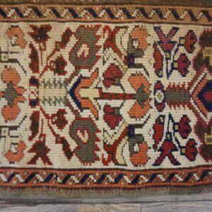 Low-pile rug section showing dense red, blue, and green geometric patterns on an ivory field over wood floor.