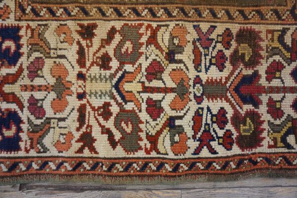 Low-pile rug section showing dense red, blue, and green geometric patterns on an ivory field over wood floor.