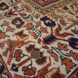 Close-up of a knotted rug showing angular motifs in cream, terracotta, navy blue, and dark brown.