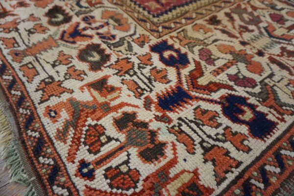 Close-up of a knotted rug showing angular motifs in cream, terracotta, navy blue, and dark brown.