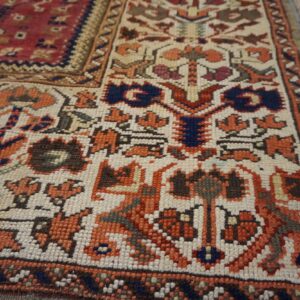 Geometric low-pile rug featuring red, orange, and blue tribal motifs on a cream field over gray wood flooring.