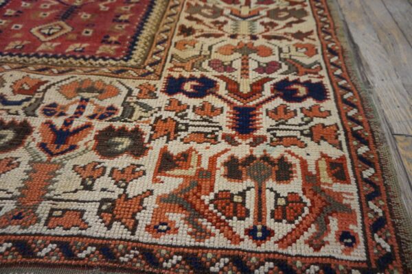 Geometric low-pile rug featuring red, orange, and blue tribal motifs on a cream field over gray wood flooring.