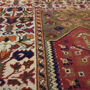 The rug features geometric ivory and rust motifs contrasting with a dense red and olive green field.