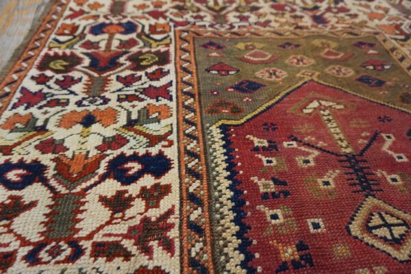 The rug features geometric ivory and rust motifs contrasting with a dense red and olive green field.