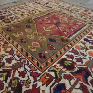 Low-pile rug with a red and olive geometric medallion and colorful patterns on a rustic wood floor.
