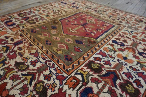Low-pile rug with a red and olive geometric medallion and colorful patterns on a rustic wood floor.