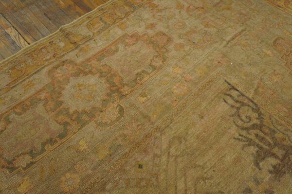 Antique oversized oushak turkish medallion knotted rug 2 Low pile beige rug with faded green and pink oriental motifs resting on plank wood flooring.