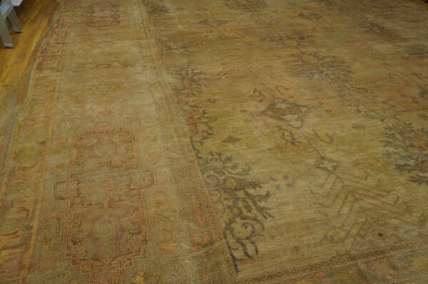 Antique oversized oushak turkish medallion knotted rug 3 Ornate gold and olive rug with faded traditional patterns covers hardwood flooring.