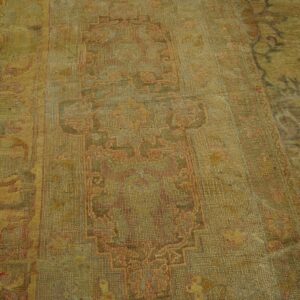 Muted gold and pink low-pile traditional rug with geometric patterns, partially shown on wood floor.