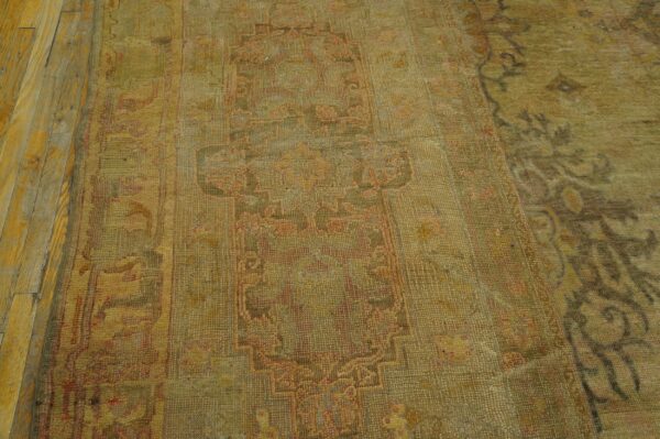 Antique oversized oushak turkish medallion knotted rug 4 Muted gold and pink low-pile traditional rug with geometric patterns, partially shown on wood floor.