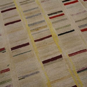 High-pile beige rug with multicolored short blocks of red, yellow, gray, and black in a striped pattern.