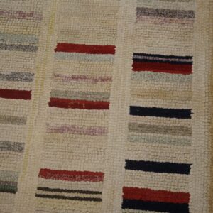 Nubbly cream rug featuring colorful horizontal blocks of red, navy, gray, and purple beside wooden planks.