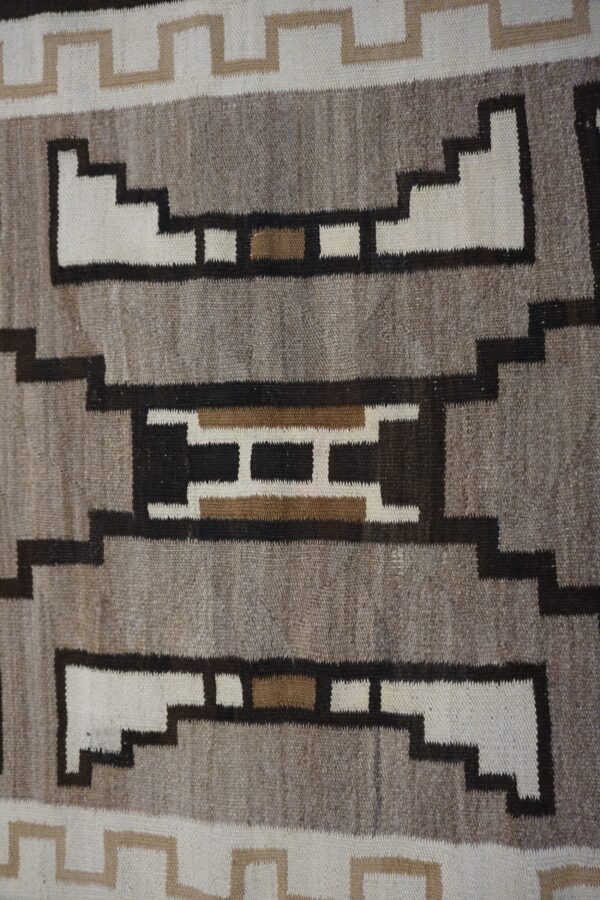 Geometric flatweave rug texture featuring stepped shapes in natural gray, white, dark brown, and tan.