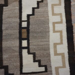 Geometric flatweave rug detail in brown, cream, and gray stepped designs rests on distressed wood planks.