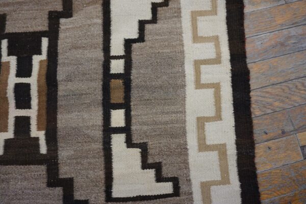 Geometric flatweave rug detail in brown, cream, and gray stepped designs rests on distressed wood planks.