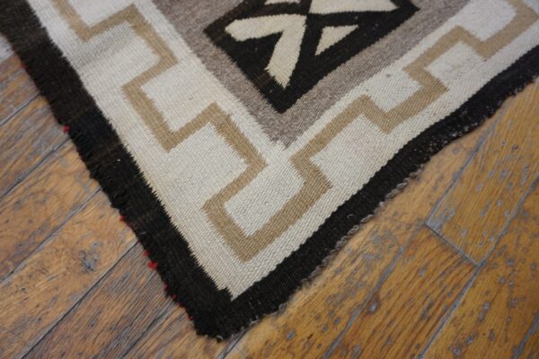 Low-pile geometric rug corner in cream, tan, and dark brown resting on distressed wood flooring.
