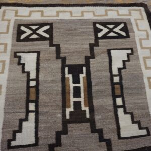 Flatweave rug featuring a stepped geometric design in brown, white, tan, and gray on distressed wood flooring.