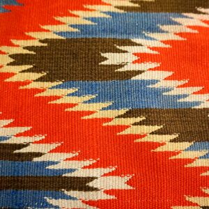 Flatweave rug detail showing bold geometric patterns in orange, blue, brown, and cream colors.