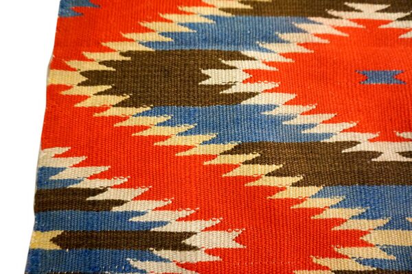 Flatweave rug detail showing bold geometric patterns in orange, blue, brown, and cream colors.