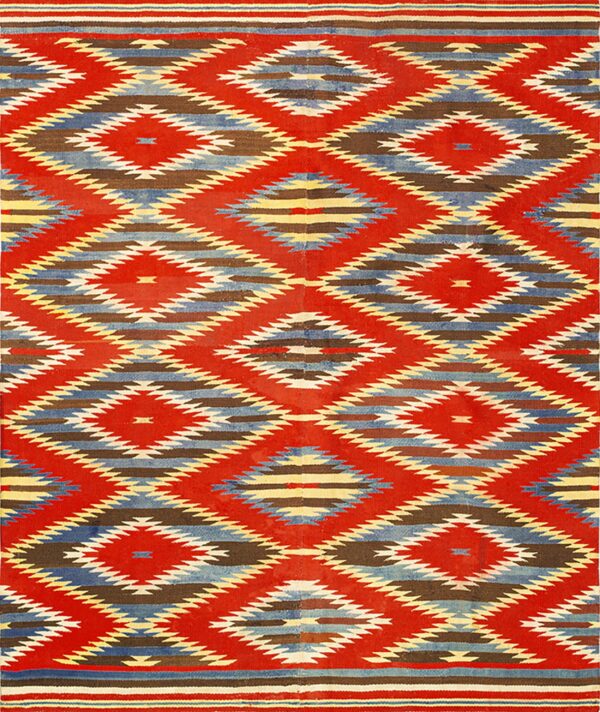 Red flatweave rug featuring geometric interlocking diamond patterns in blue, brown, yellow, and cream.