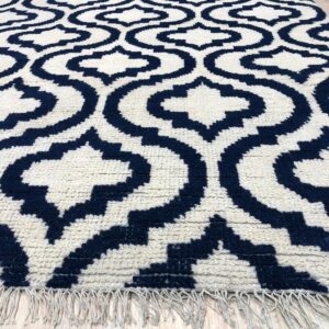 Textured navy and cream rug with a geometric ogee pattern, visible fringe, on light wood planks.