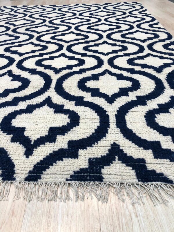 Textured navy and cream rug with a geometric ogee pattern, visible fringe, on light wood planks.