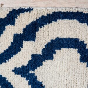 Shaggy ivory rug with a thick navy blue geometric pattern and fringe on light wood floorboards.