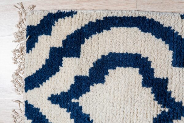 Shaggy ivory rug with a thick navy blue geometric pattern and fringe on light wood floorboards.