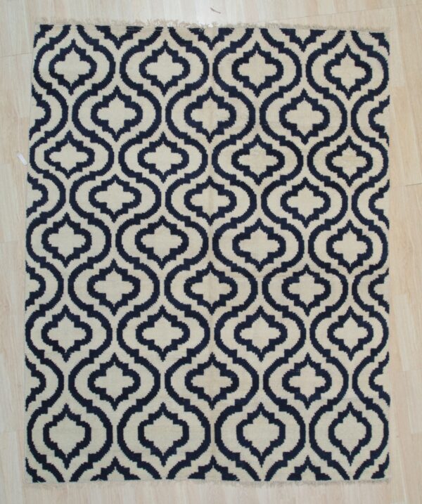 Navy and cream rug with an interlocking geometric pattern, laid flat on light wood planks.