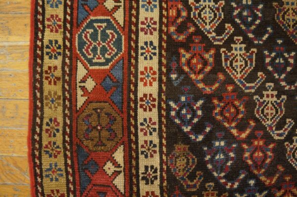 Detailed view of a low-pile rug with geometric patterns in dark, red, blue, and tan on wood floors.
